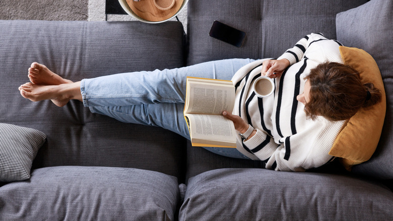 A woman on the couch with a book and a cup of coffee, seen from above