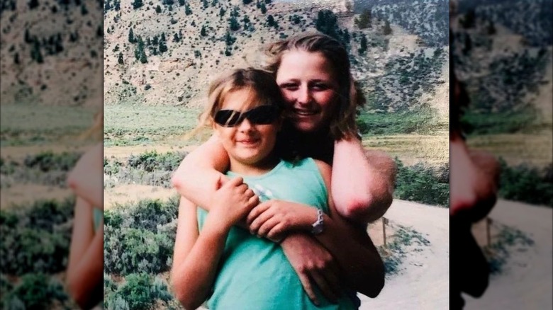 Old photo of young Louisa Jacobson being embraced by her older sister Mamie Gummer in front of a mountainous background
