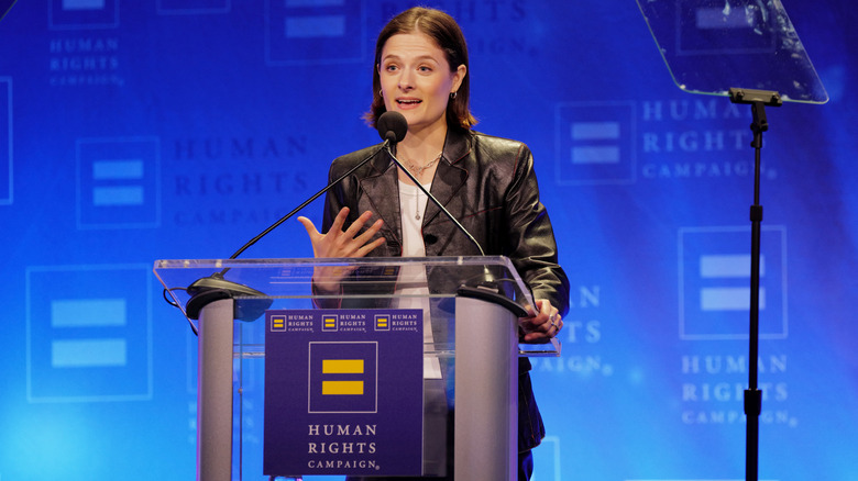Louisa Jacobson speaking at the Human Rights Campaign 2025 Greater New York Dinner while wearing a leather jacket and shoulder-length cut