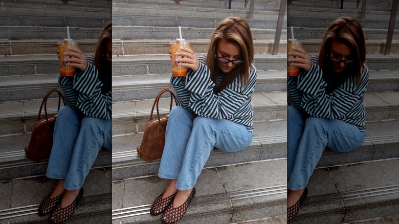 Image of style influencer holding a drink and posing for a photo in a micro striped long sleeve t-shirt, light wash jeans, and jelly shoes