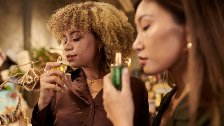 Two women smelling bottles of perfume