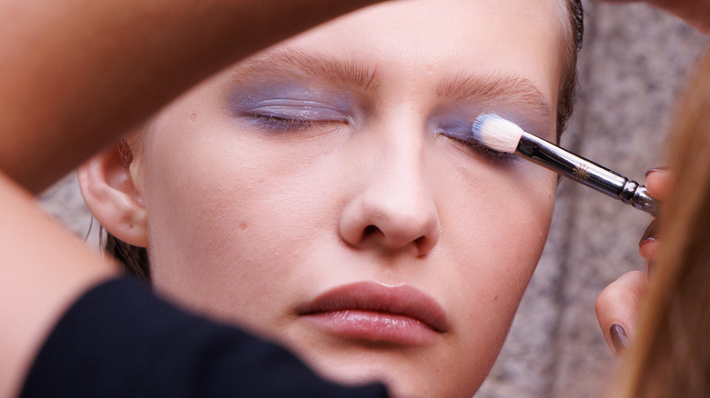 A woman applying light purple eyeshadow to a model's eyelid