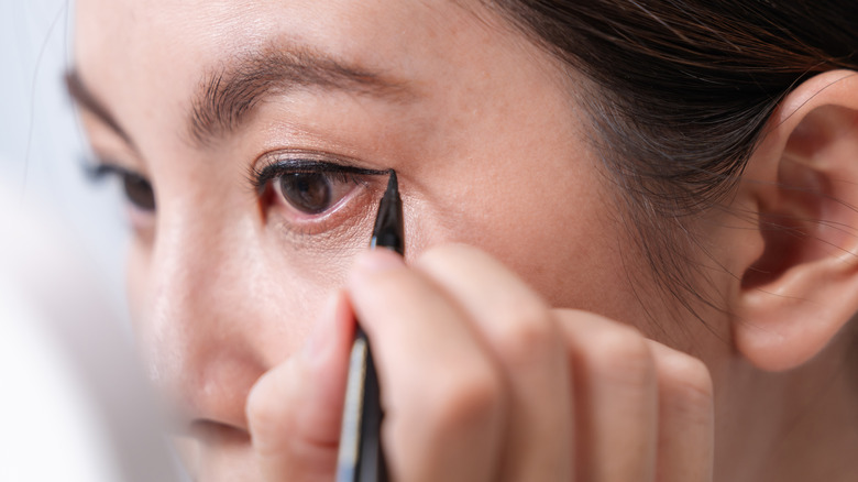 A woman applying winged eyeliner with a pen
