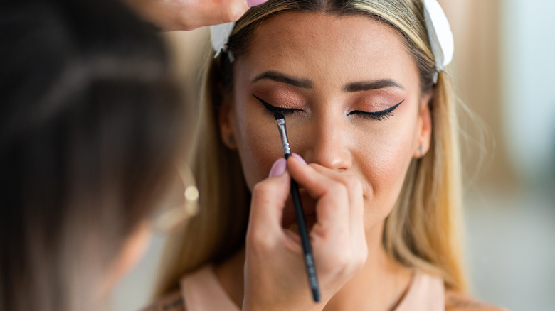 A woman applying eyeshadow with a brush to another woman's eyelid