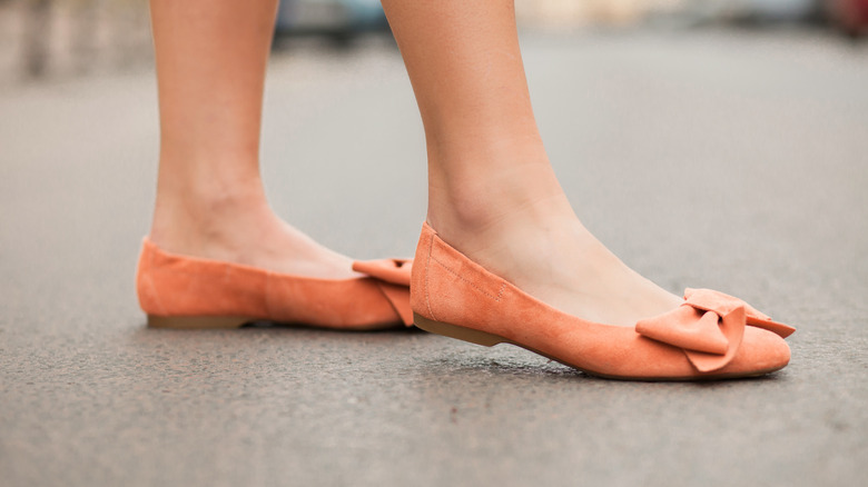 A woman's feet in orange ballet flats with bows on the toes
