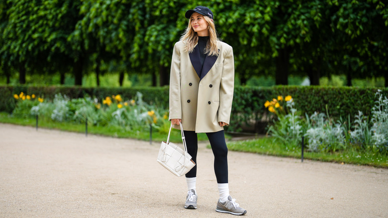 A woman in leggings with a cream blazer and white sneakers