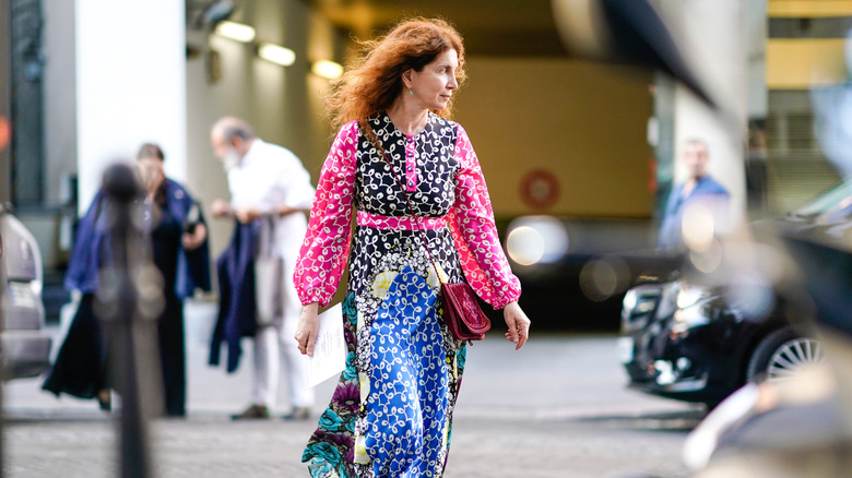A guest wears a pink, black and blue flower print dress, a red bag, outside Valentino, during Paris Fashion Week Haute Couture Fall Winter 2018/2019, on July 4, 2018 in Paris, France
