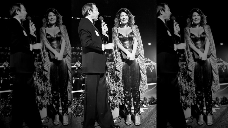 Black-and-white photo of Raquel Welch being interviewed on the red carpet at the 1979 Oscars in a sequin jumpsuit