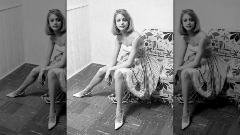 Goldie Hawn sits wearing pointed white heels and a gingham dress