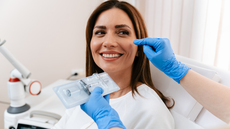 A young woman smiling while doctor holds tray of filler