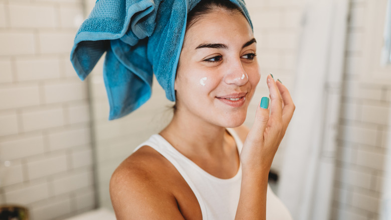 A woman with a blue towel on her head applying cream