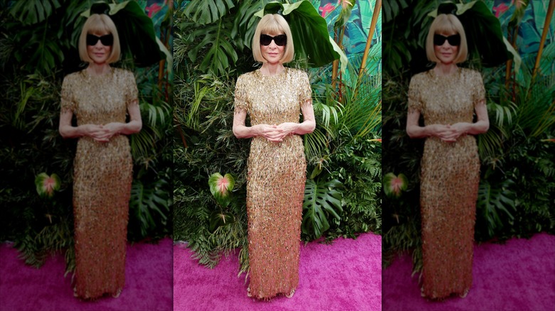 Anna Wintour poses wearing a gold sequin dress and black sunglasses