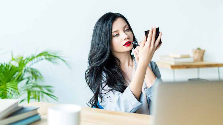 Woman applying red lipstick in her office