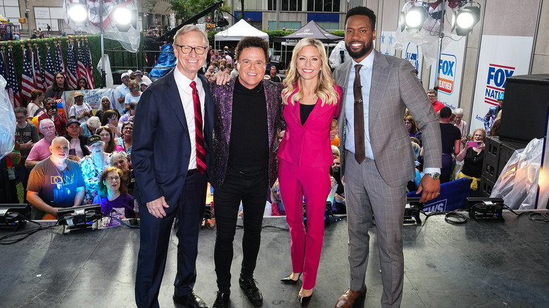 Ainsley Earhardt in a fuschia pantsuit posing with Donny Osmond
