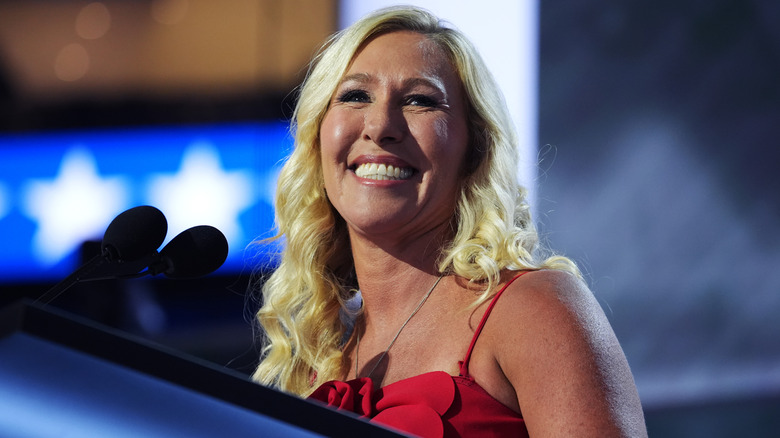Marjorie Taylor Greene smiles as she stands on stage