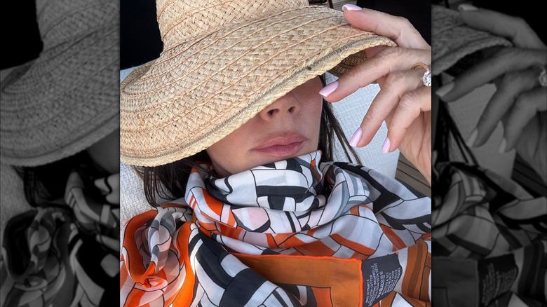 Victoria Beckham lying down while holding up her hat