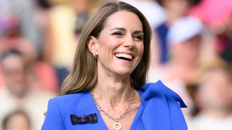 Kate Middleton smiling while wearing a blue dress while standing in front of a crowd
