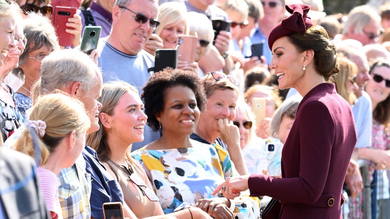 Kate Middleton, in a burgundy hat and coat, speaking with fans
