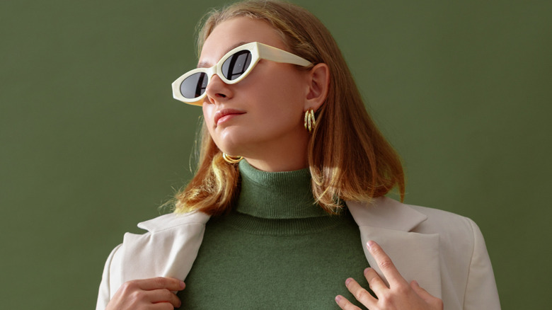 Woman wearing white sunglasses, green turtleneck, and beige suit