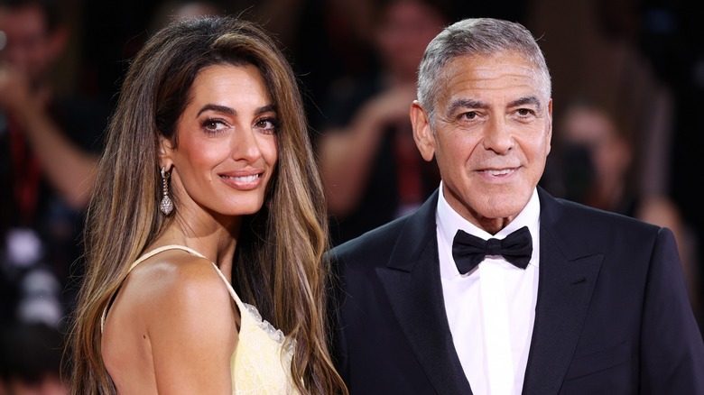 Amal Clooney smiling next to George Clooney on the red carpet