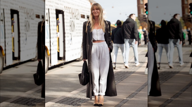 A woman wearing a leather trench coat and sweat pants 