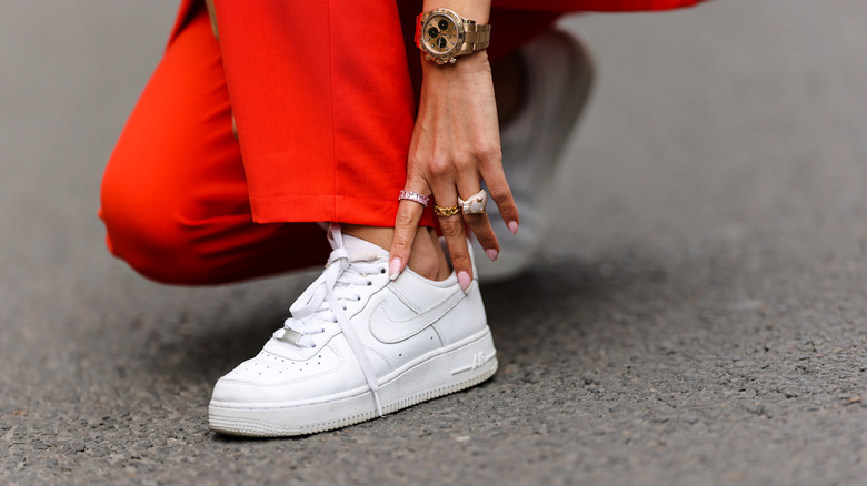 Woman with a watch and rings on touching white sneakers 
