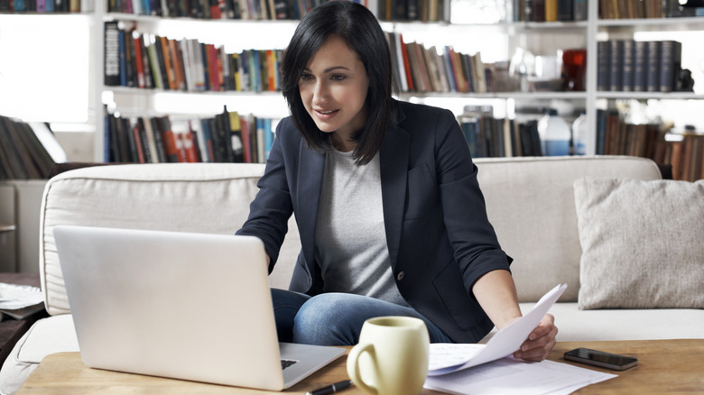 Woman holding papers and looking at laptop