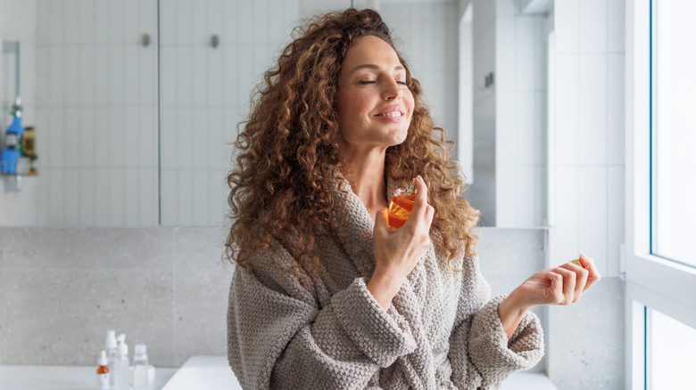Young woman closing her eyes and sniffing a perfume bottle