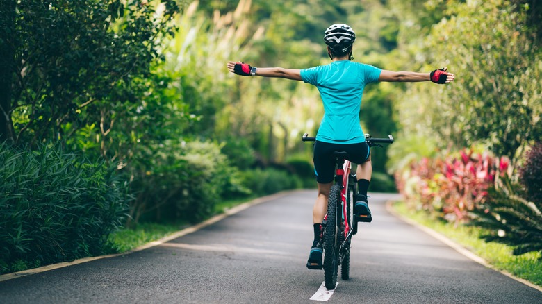 Woman cycling arms outstretched woods