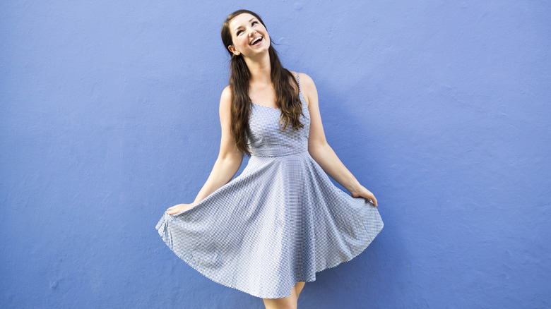 A woman wearing a blue sundress and standing in front of a blue wall