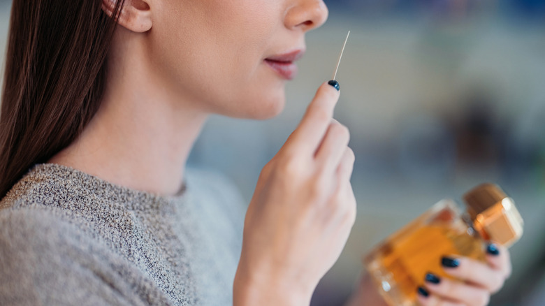 A woman sniffing a test strip from a perfume bottle that she's holding in her other hand