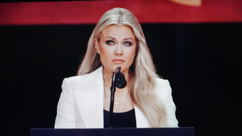 Erika Kirk at a podium in a white suit