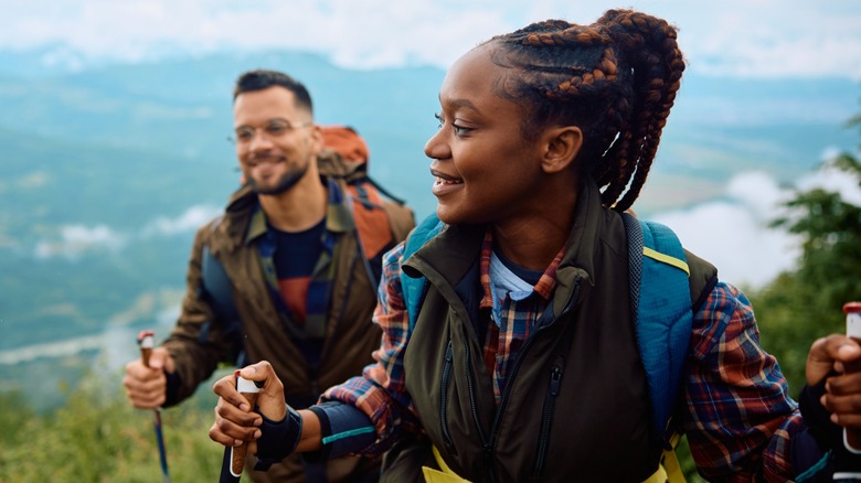 A woman hiking up a tall mountain with a man smiling behind her