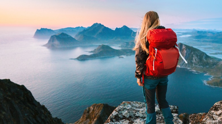 A lone woman looking over a high cliff wearing a red backpack