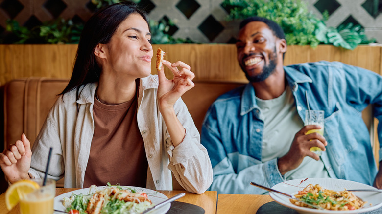 Happy couple enjoying a casual dinner date, smiling and eating delicious food in a modern restaurant