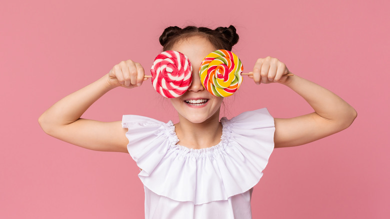 a little girl holding lollipops up to her eyes 