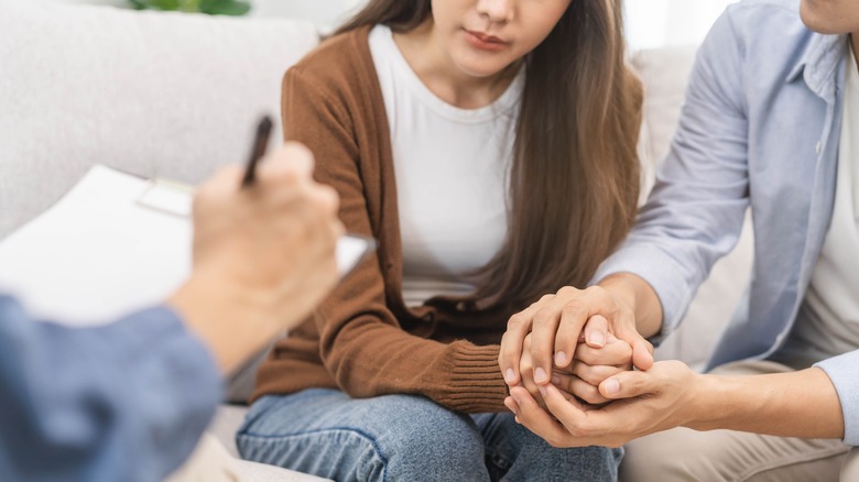 Man holding woman's hands while doctor fills out form