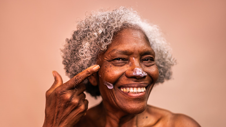 An elderly woman grins as she applies suncream