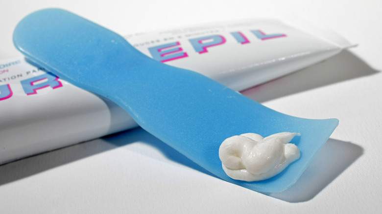 Close-up of blue spatula applicator holding a squirt of hair removal cream