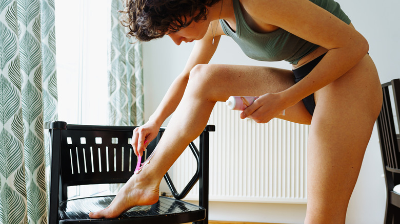 Young woman applying hair removal scream to her leg with a spatula