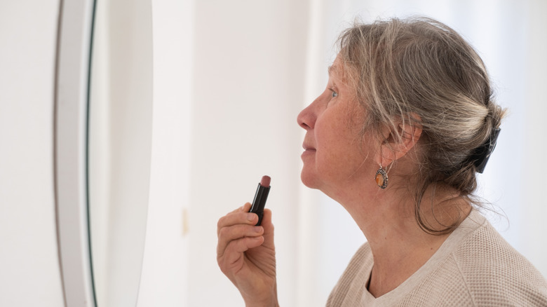 An older woman applying lipstick in the mirror
