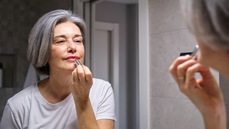 An older woman applying lipstick in the mirror
