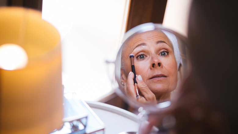 An older woman uses a mirror to help her apply makeup