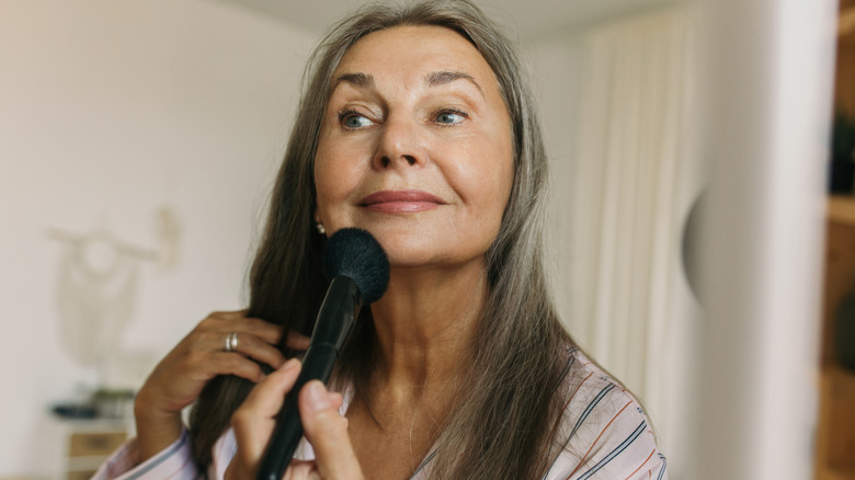 An older woman applying makeup using a brush