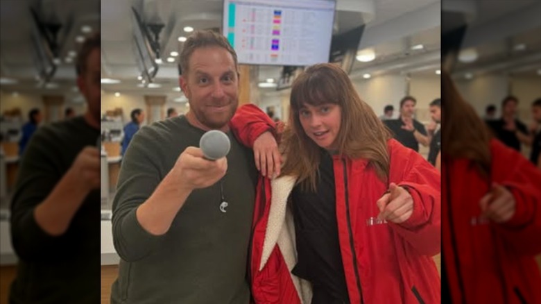 Fiona Dourif wearing a red jacket and standing next to a man holding out a microphone