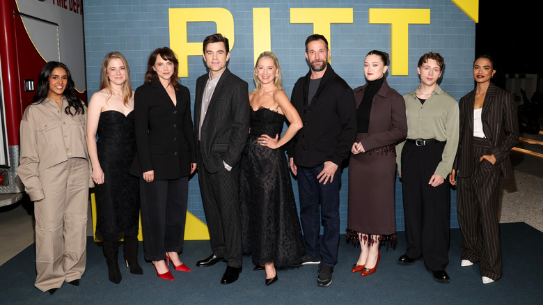 The cast of The Pitt standing in front of a step and repeated that says 