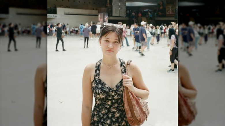 A photo of Isa Briones standing in a plaza in a dark floral top with people behind her