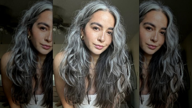 A woman with long silver hair looks into the camera