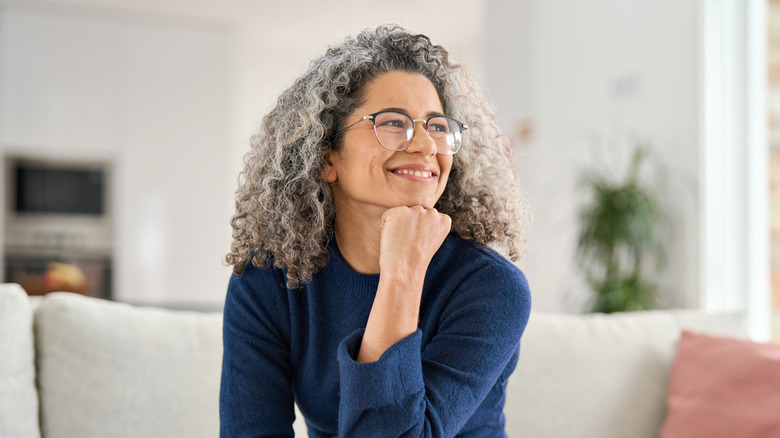 A woman with curly gray hair sits on a couch