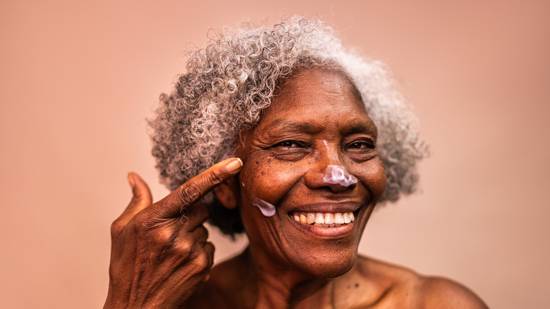 An elderly woman grins as she applies suncream